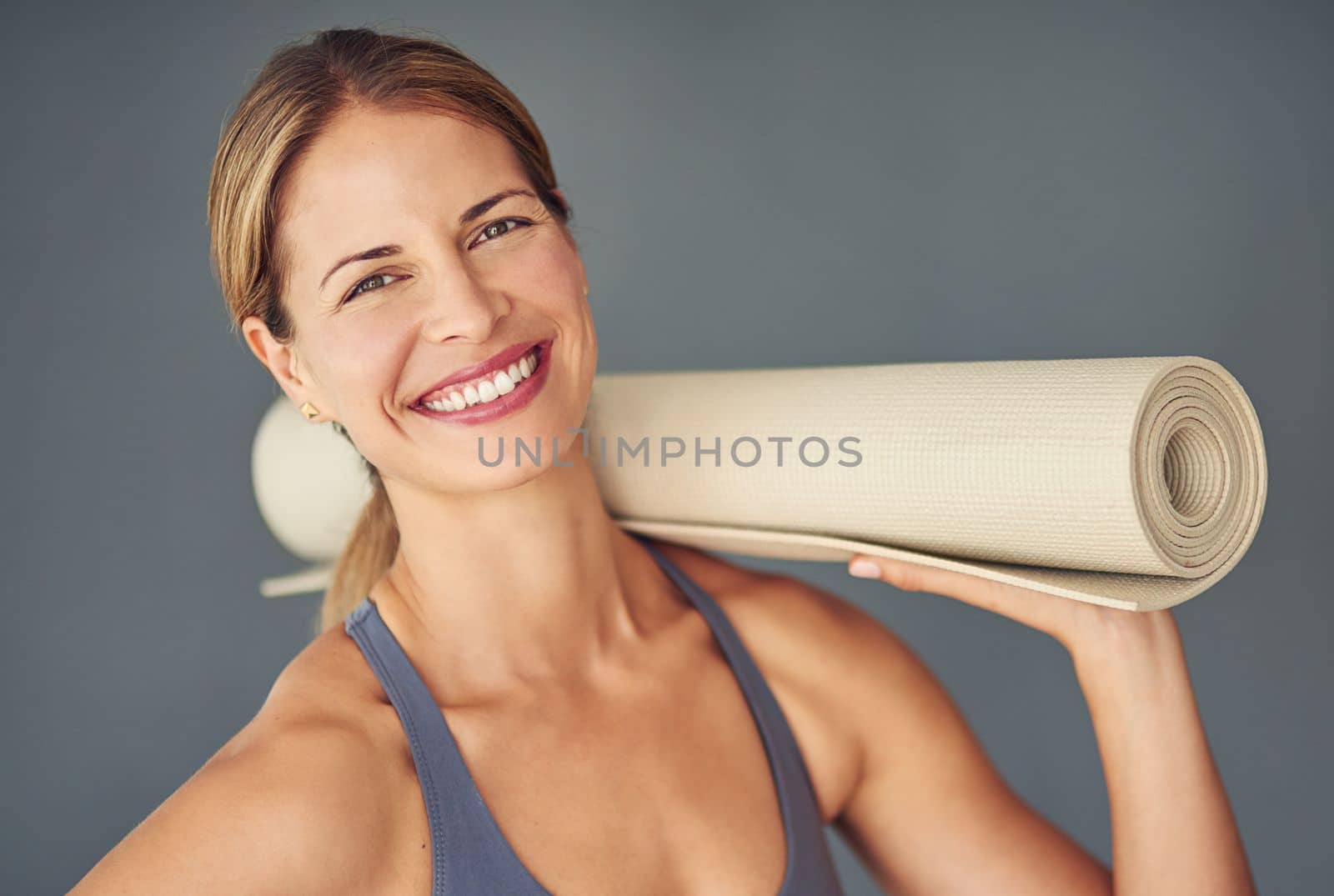 Yoga gives you more energy. a woman holding her yoga mat against a grey background. by YuriArcurs