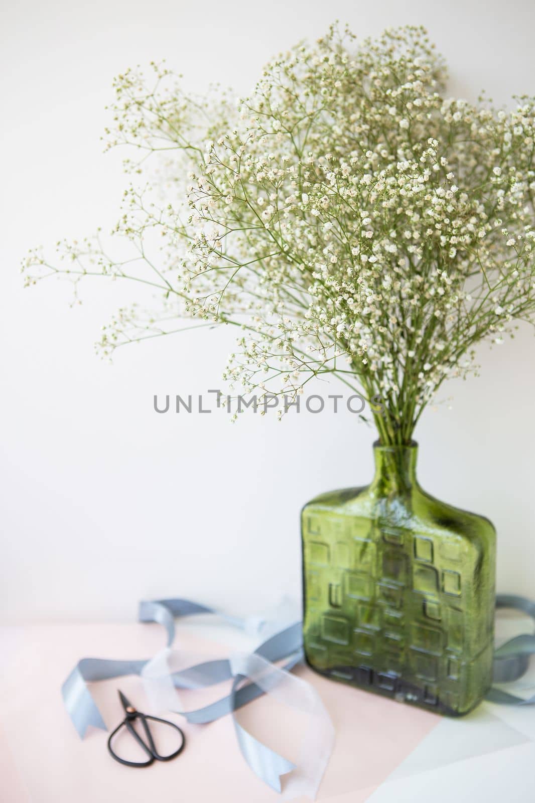 Preparing the bouquet for the wedding ceremony, a bouquet of white gypsophila flowers stands in a green vase along with ribbons and scissors