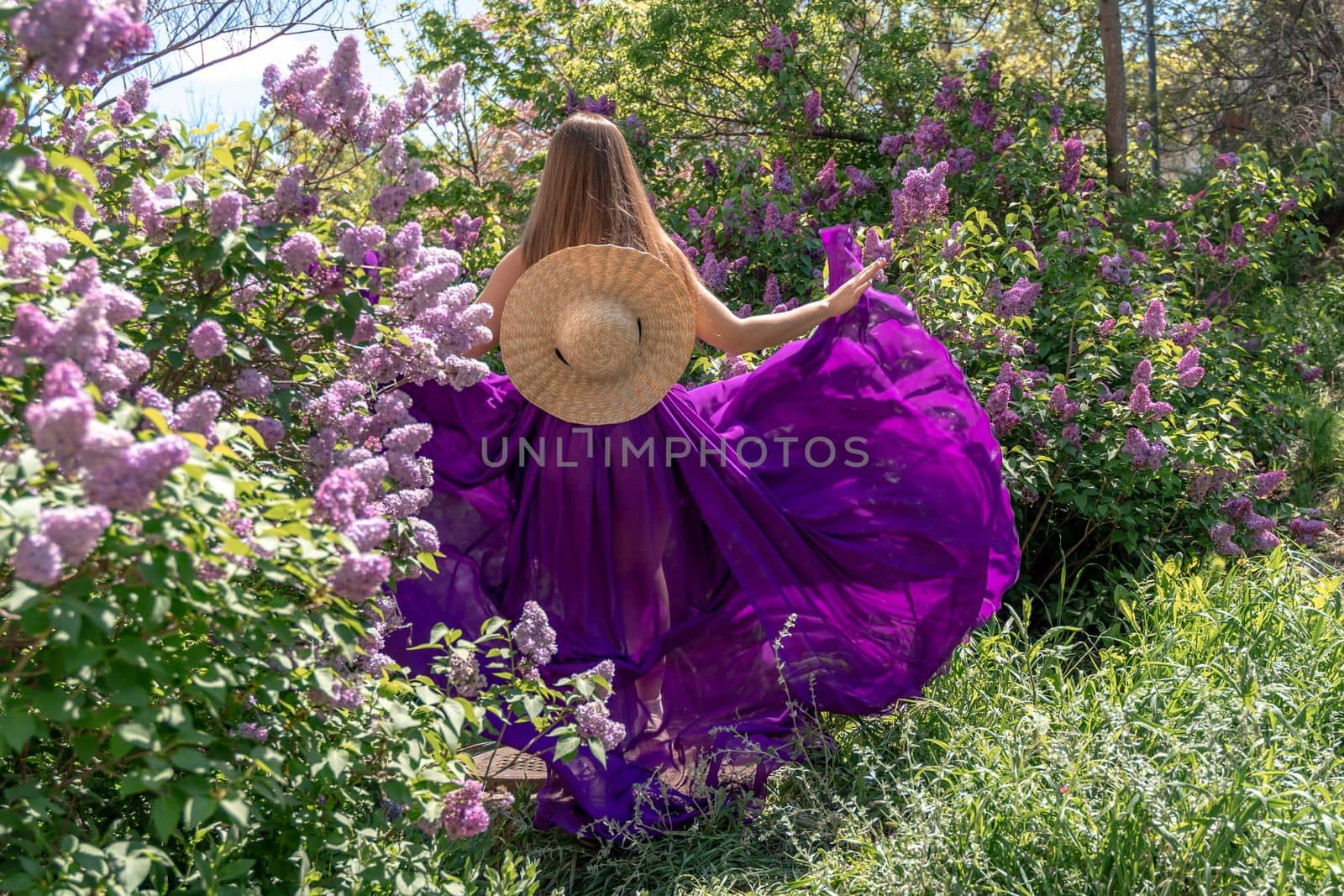 Fashion Model in Lilac Flowers, Young Woman in Beautiful Long Dress Waving on Wind, Outdoor Beauty Portrait in Blooming Garden.