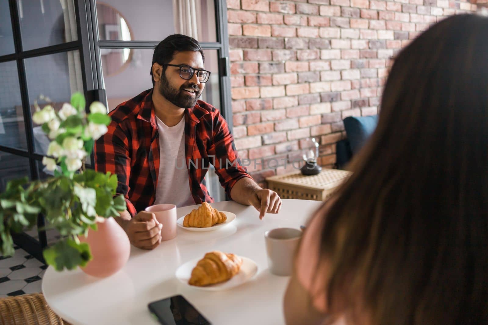 Young diverse loving couple eating croissant and talks together at home in breakfast time. Communication and relationship concept by Satura86