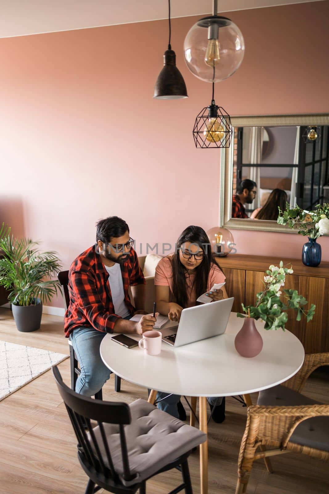 Serious wife and husband planning budget, checking finances, focused young woman using online calculator, counting bills or taxes, man using laptop, online banking services. Family sitting at table in kitchen - economic crisis concept