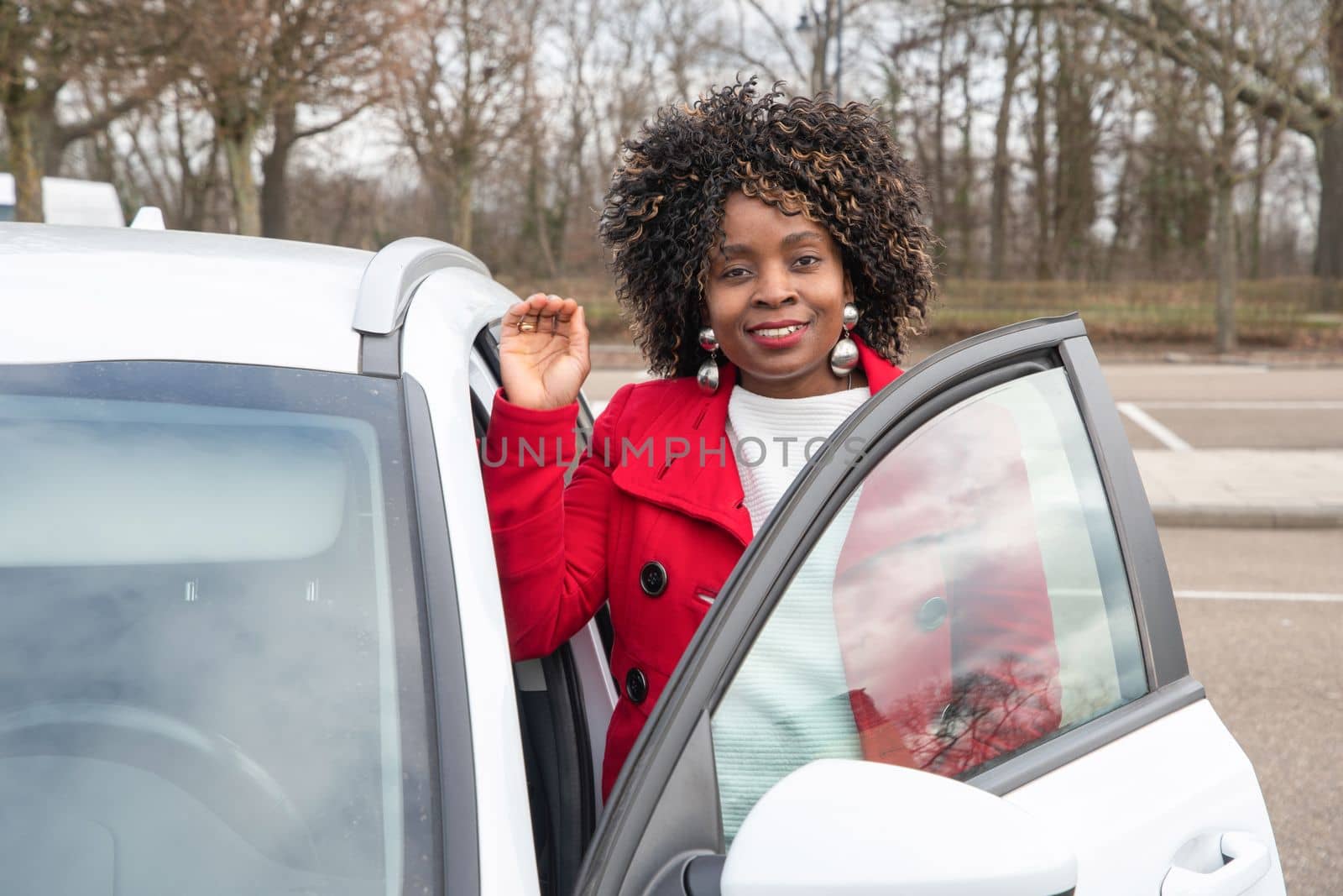 Confident african american businesswoman in red coat standing with white car by KaterinaDalemans