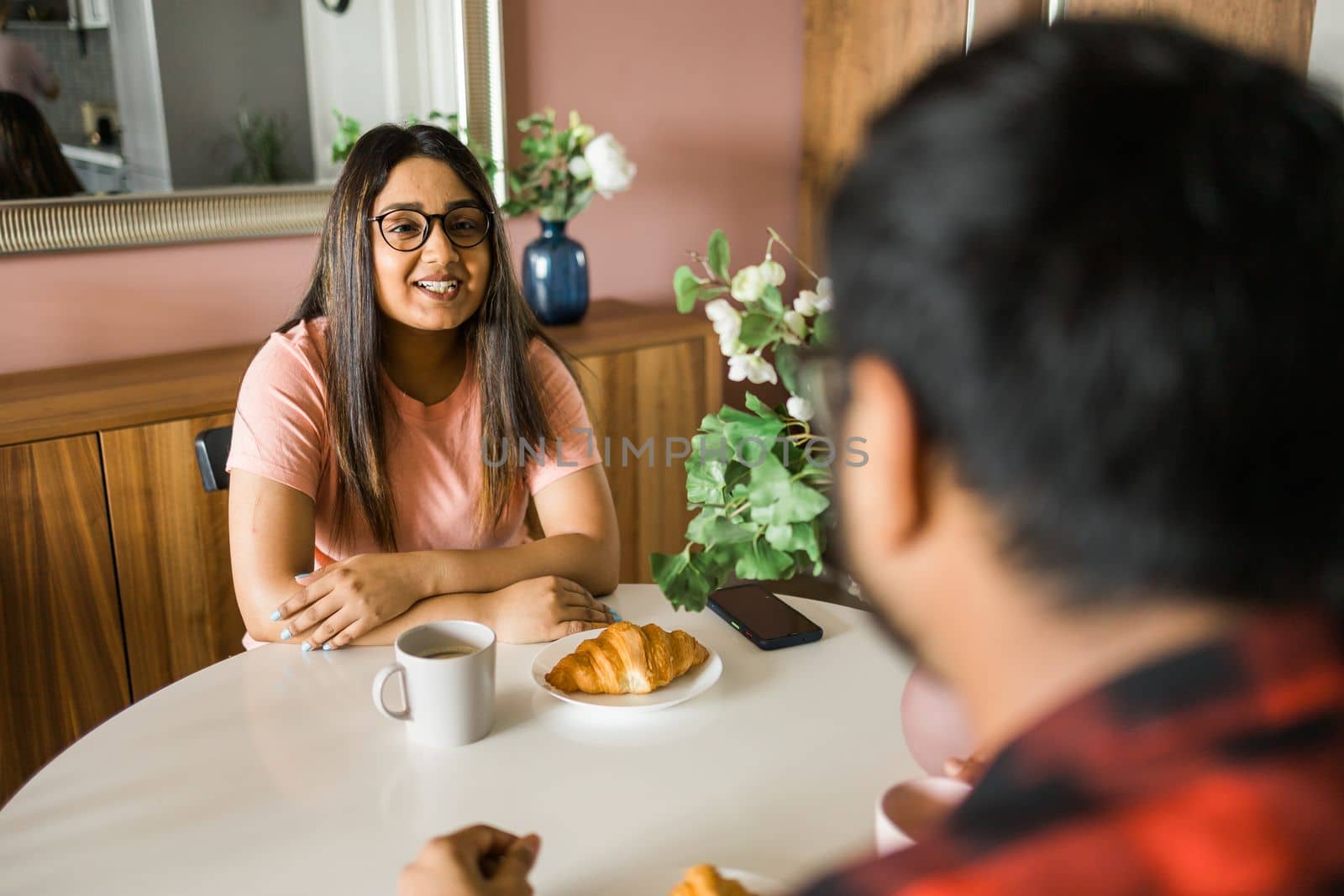 Young diverse loving couple eating croissant and talks together at home in breakfast time. Communication and relationship