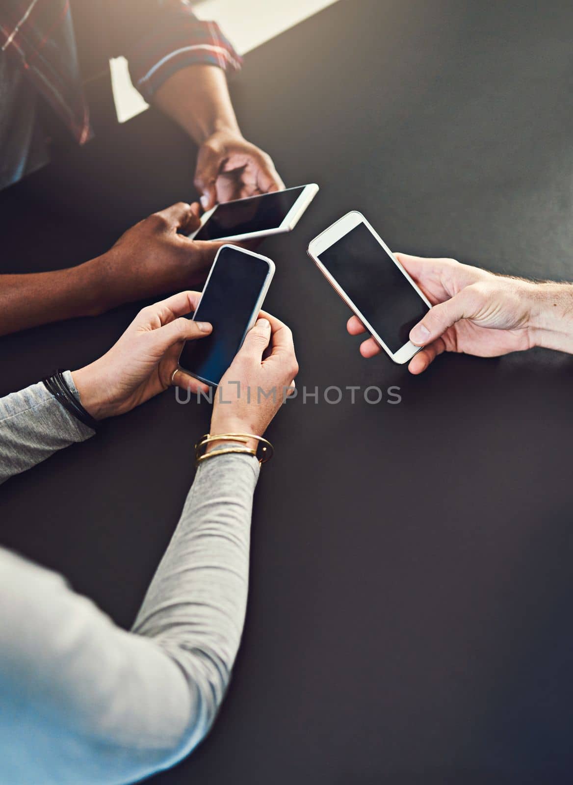 Working with technology as a team. three people sitting around a table together and using their cellphones. by YuriArcurs