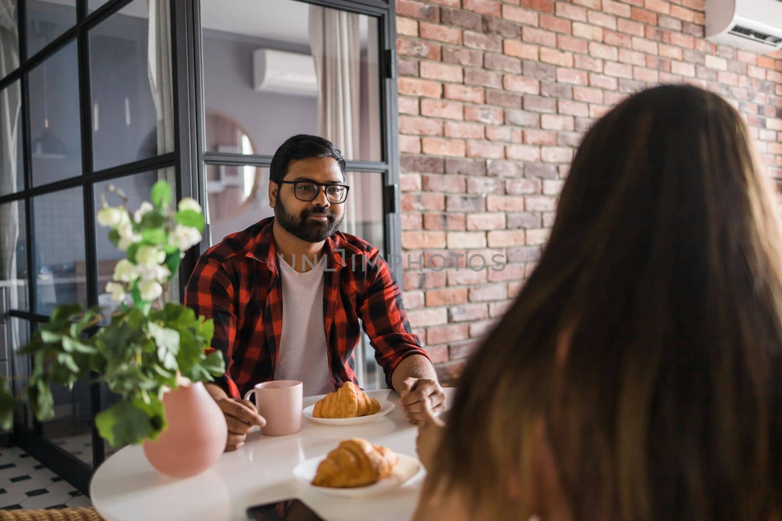 Young diverse loving couple eating croissant and talks together at home in breakfast time. Communication and relationship