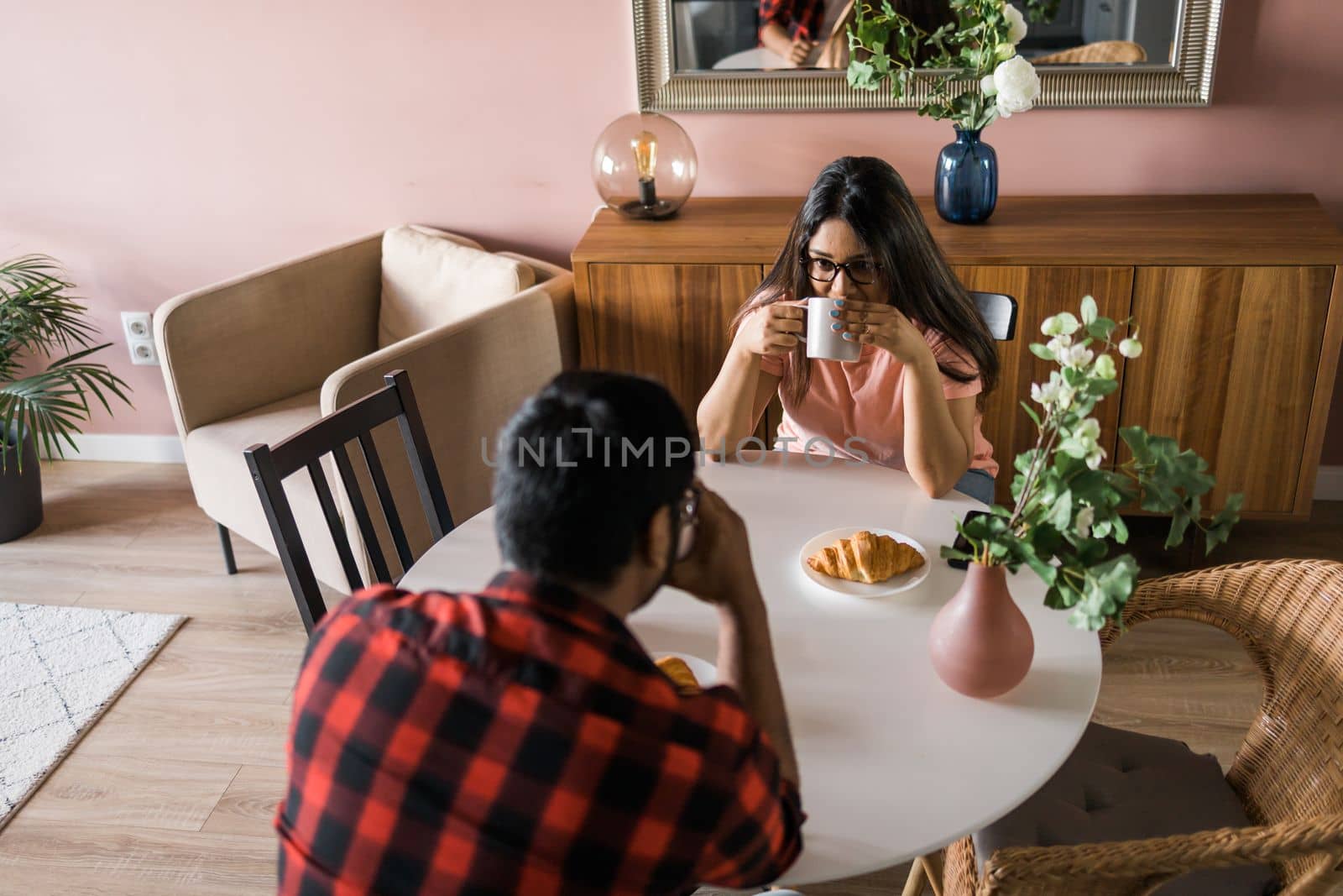 Young diverse loving couple eating croissant and talks together at home in breakfast time. Communication and relationship