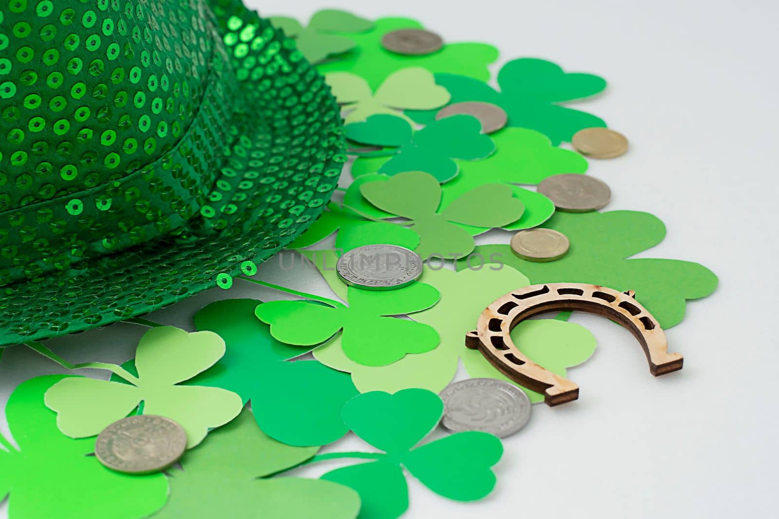 St. Patrick's Day concept. Mock-up, layout of green clover, shamrock on white background and green top hat with wooden horseshoe and metal coins Close-up. Soft focus. Irish holiday.