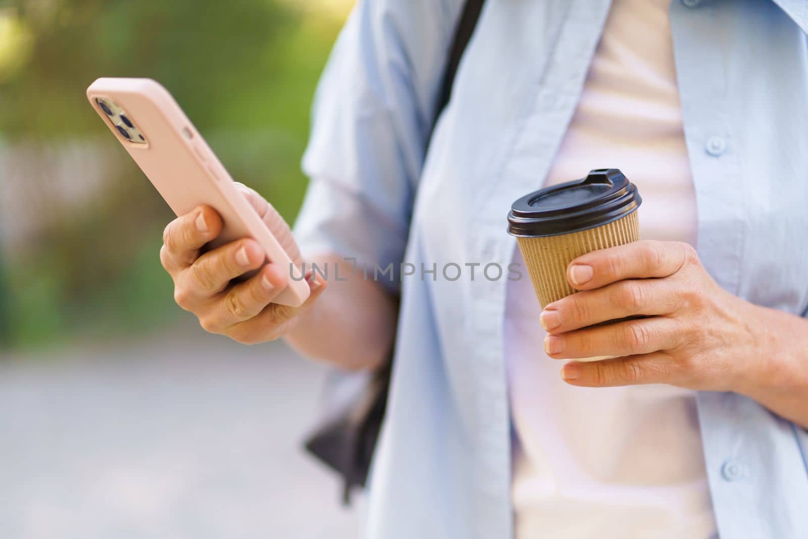 close-up photo focuses on a woman's hands holding a mobile phone and a coffee paper cup. The image depicts modern lifestyle and the widespread use of technology in daily routines. . High quality photo