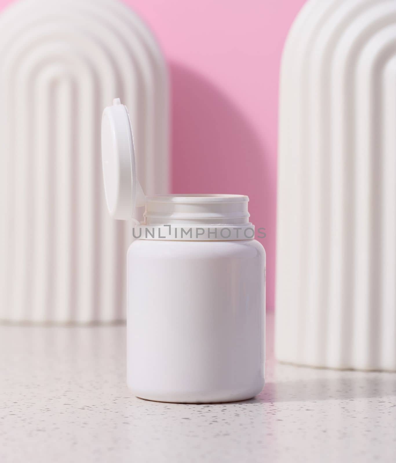 White plastic jar with an open lid for cosmetics and medical preparations on a pink background by ndanko