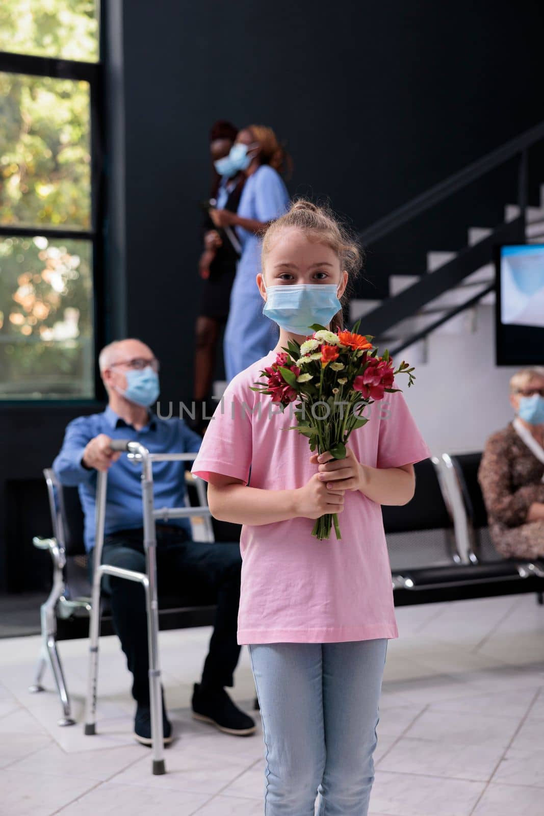 Little girl standing in hospital looby area while holding bouqet of flowers during checkup visit by DCStudio