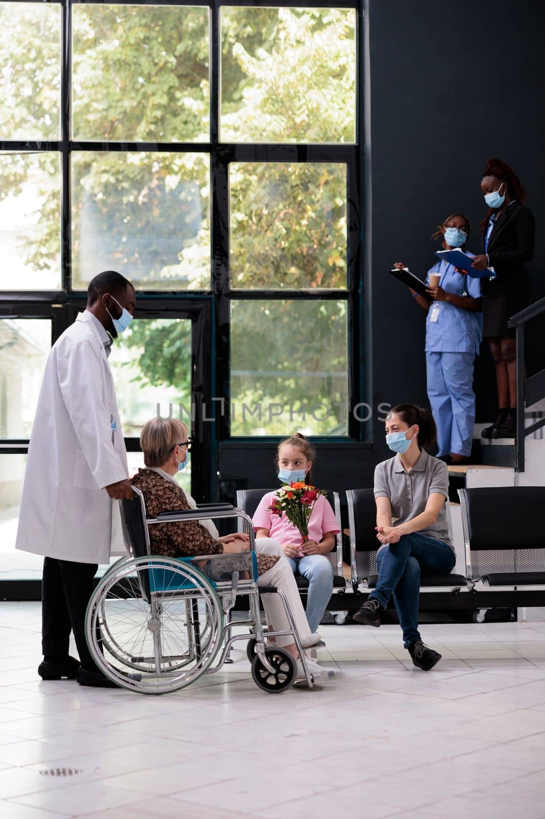 African american medic bringing disabled senior woman to family after medical consultation during checkup visit examination. Little girl holding bouquet flowers for grandmother. Virus pandemic