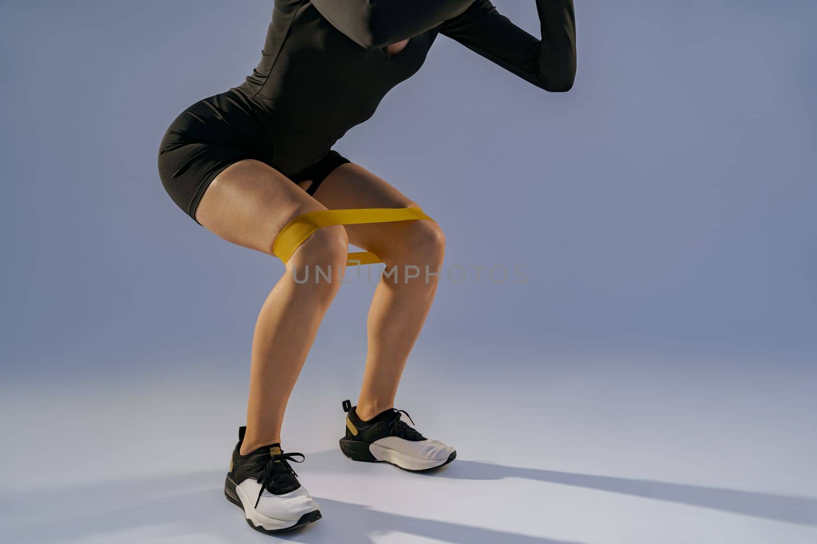 Athletic woman trains legs with fitness elastic band on studio background. High quality photo