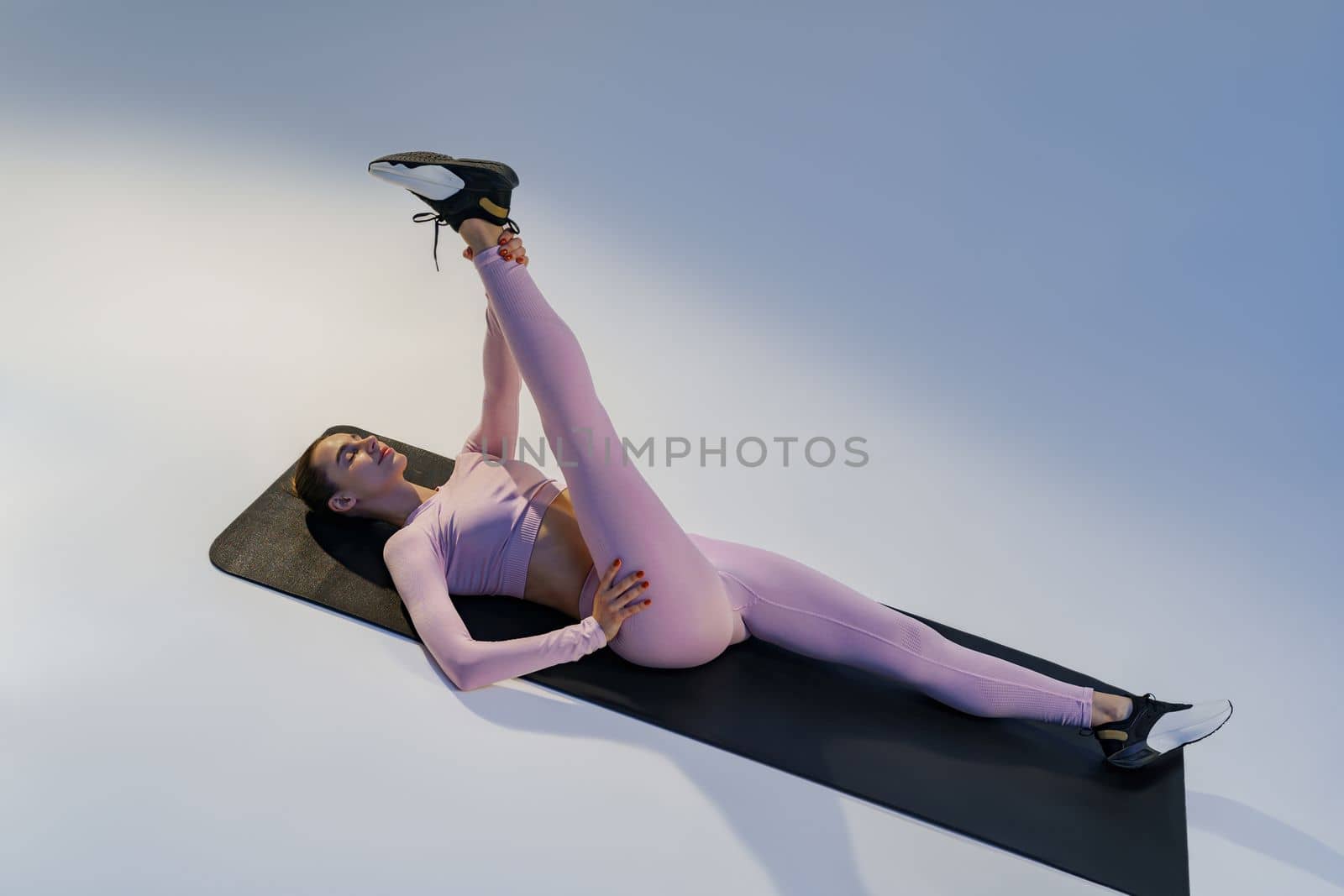 Athletic woman in sportswear doing stretching exercises on yoga mat on studio background
