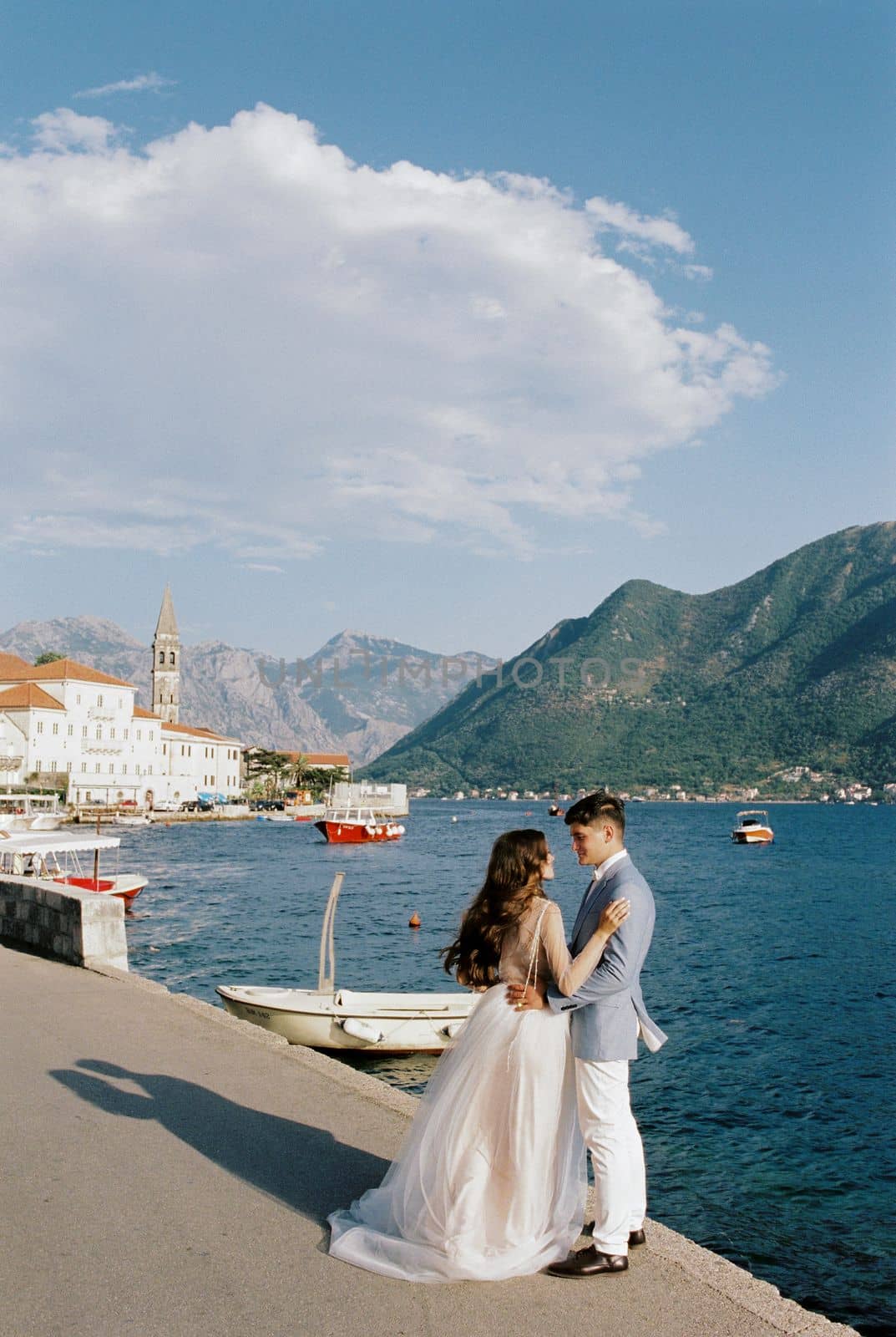 Bride and groom are standing on the Perast pier near the moored boats. High quality photo