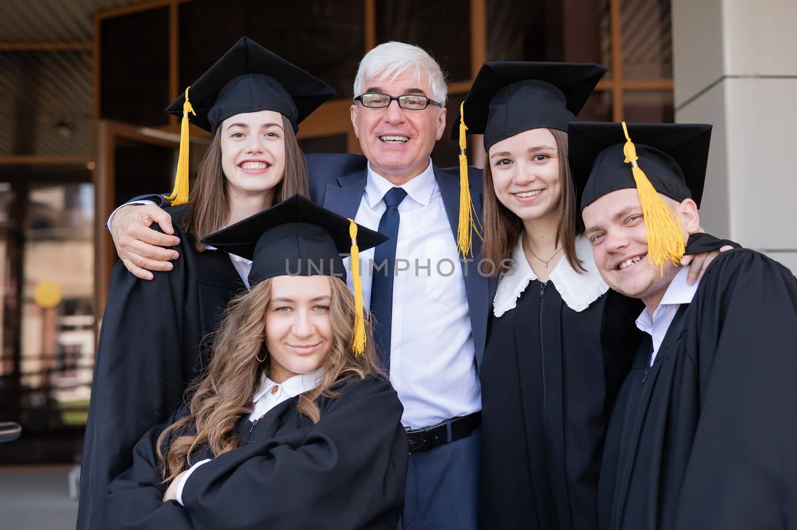 A gray-haired male teacher congratulates students on their graduation from the university