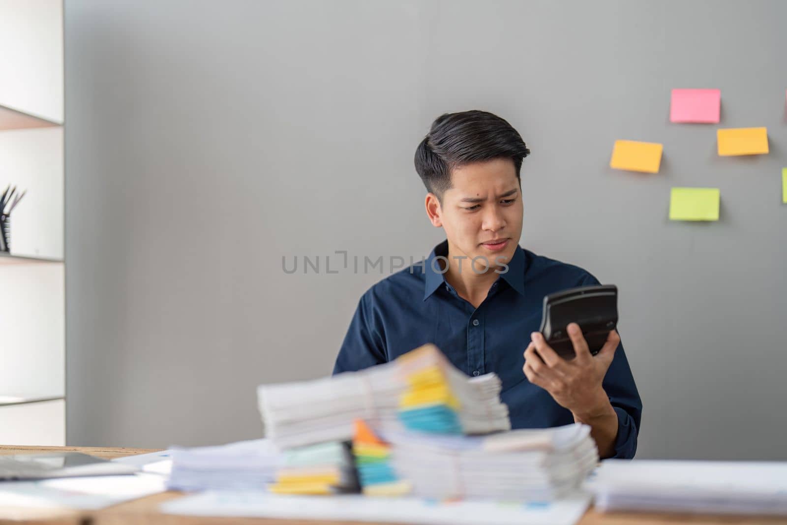 Hand of stress young asian businessman,male is pressing a calculator to calculate tax income and expenses, bills, credit card for payment or payday at home, office.Financial, finance concept by nateemee