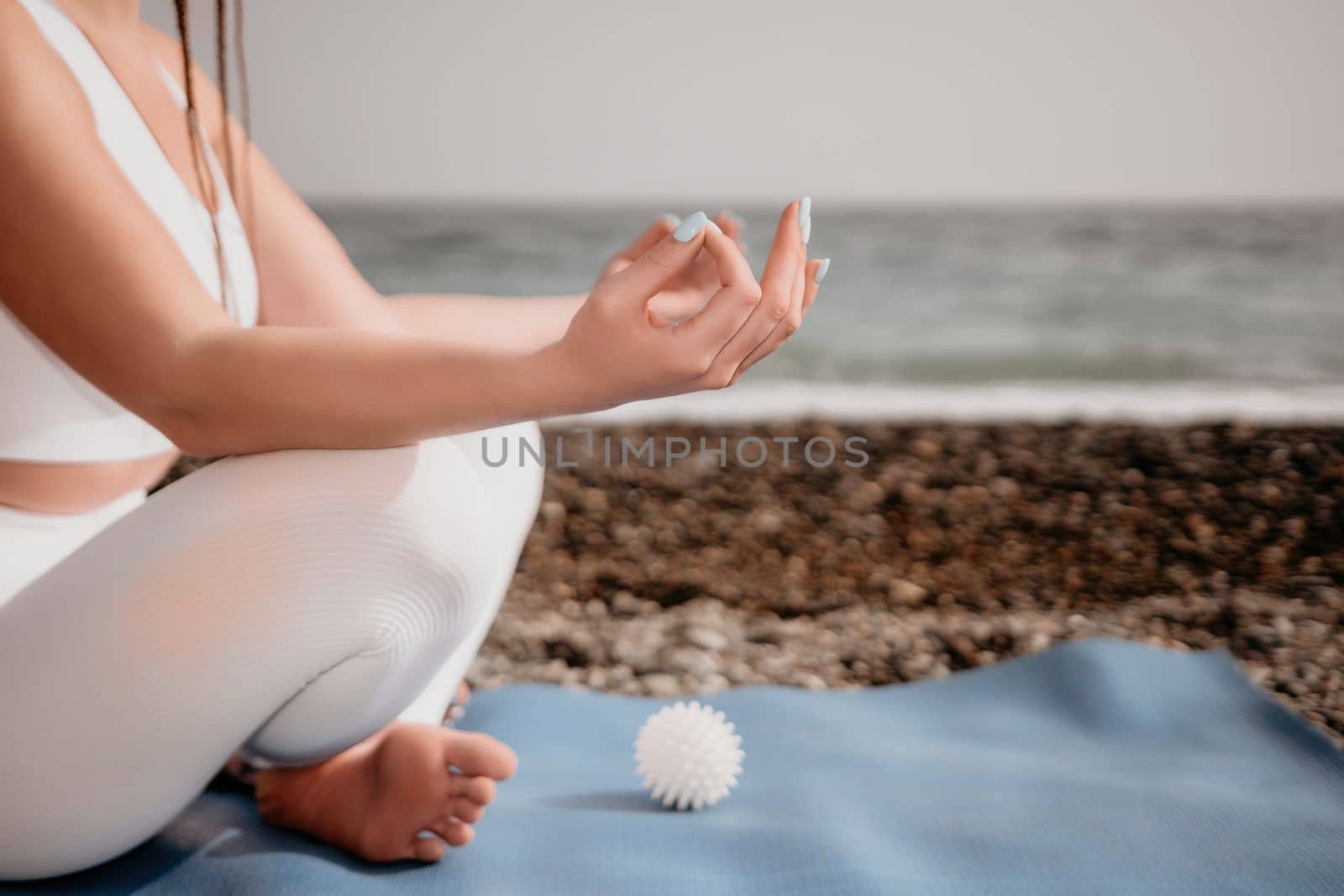 Close up Yoga Hand Gesture of Woman Doing an Outdoor meditation. Blurred sea background. Woman on yoga mat in beach meditation, mental health training or mind wellness by ocean, sea. Selective focus by panophotograph