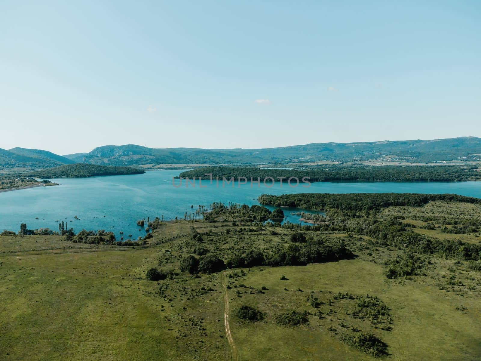 Aerial landscape from flying drone storage reservoir at mountain foot covered colorful spring forest. Beautiful view from above blue lake among highlands