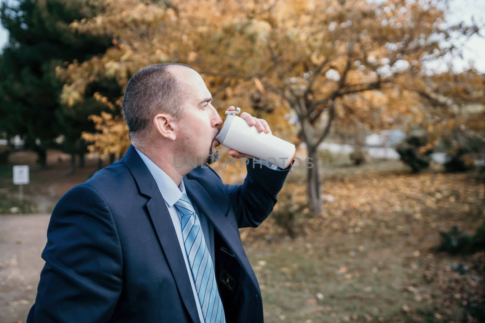 Mature entrepreneur drink coffee in autumn park. Senior executive rest in city park.