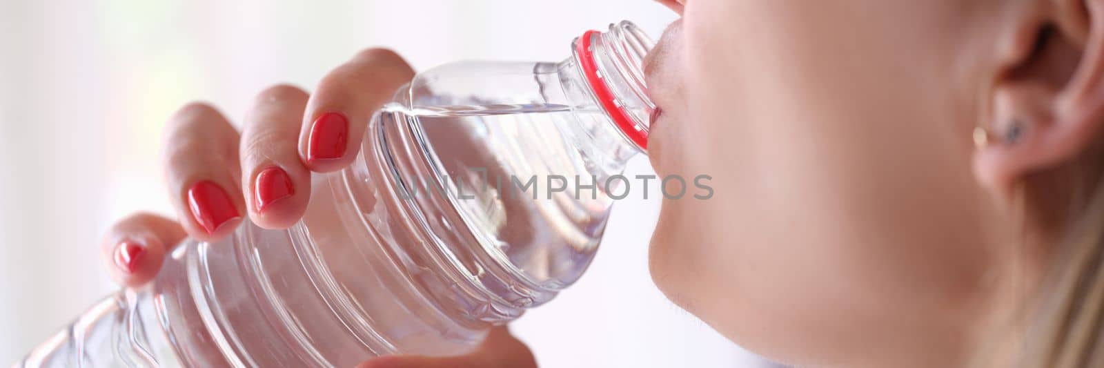 Closeup of young woman drinking water from plastic bottle. Hydration concept and cooling thirst