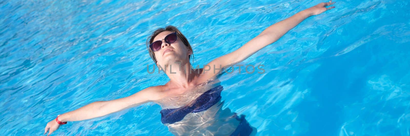 Happy beautiful woman in sunglasses relaxing in pool water. Relaxed woman in swimsuit floating in water