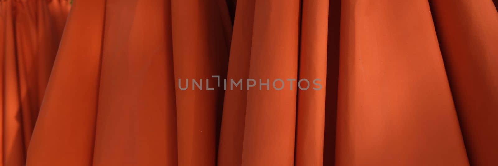 Red orange umbrellas stand stacked on beach. Sun protection equipment for beach