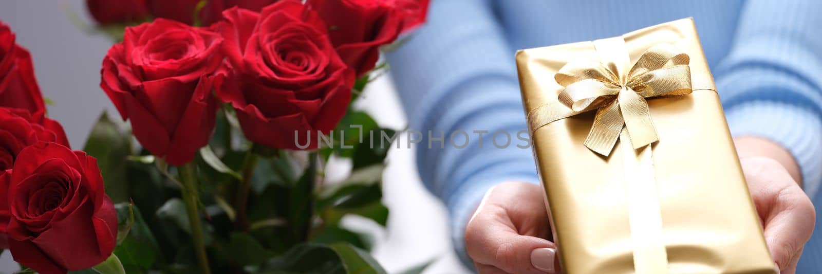 Bouquet of red roses and golden gift box in hands of courier. Delivery of romantic gifts concept