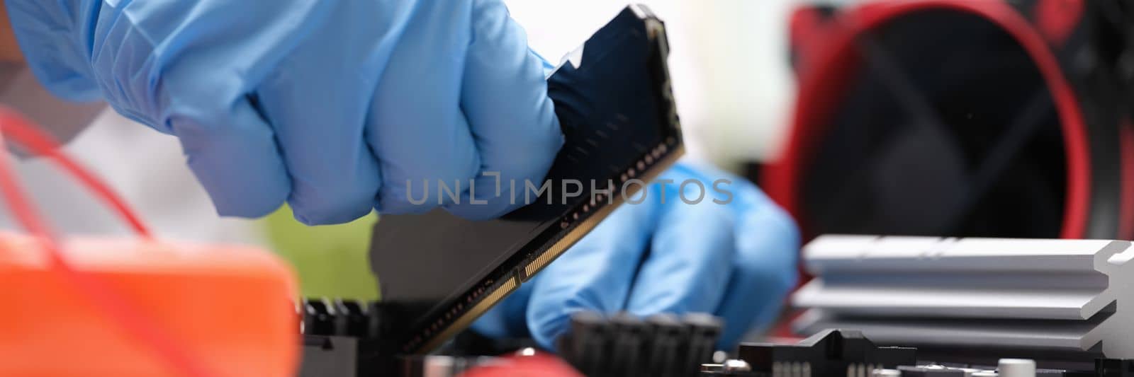 Repair engineer holds RAM chip with hands and inserts RAM of computer into socket of computer motherboard by kuprevich