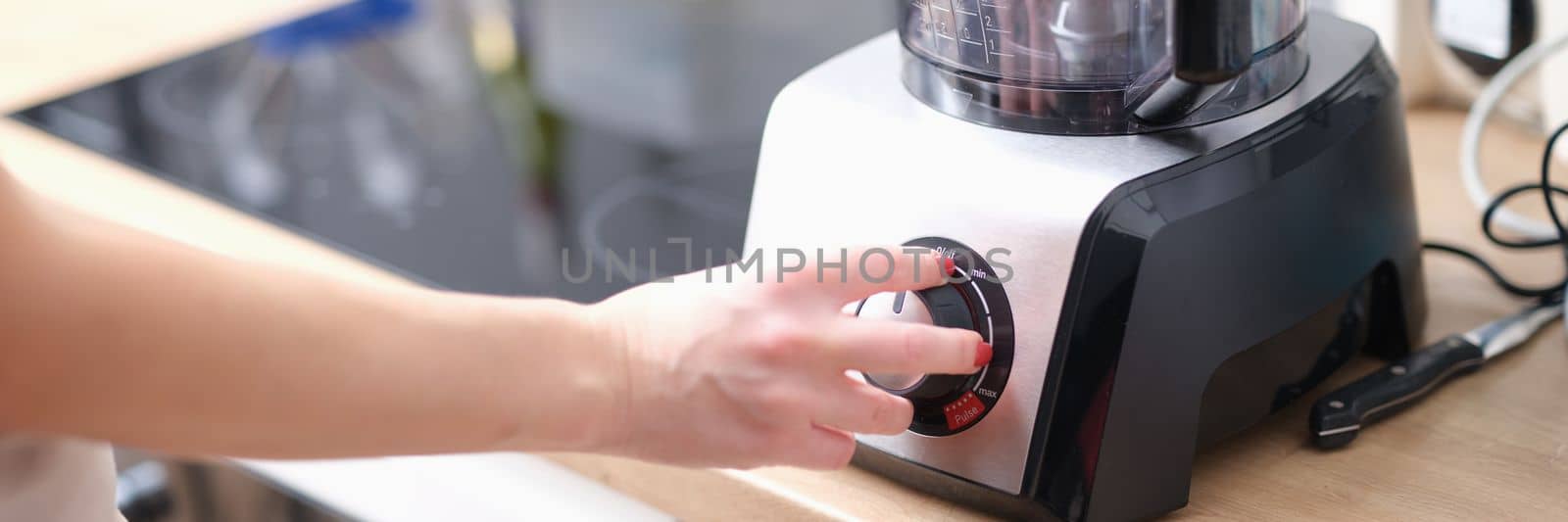 Woman switches button on electric blender in kitchen. Kitchen appliances for chopping and mixing food concept