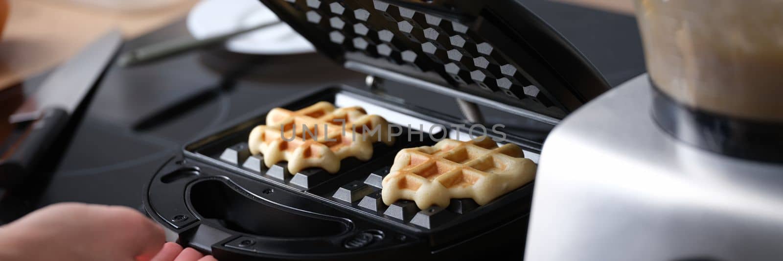 Woman prepares homemade Belgian waffles in kitchen. Closeup waffle iron and breakfast concept