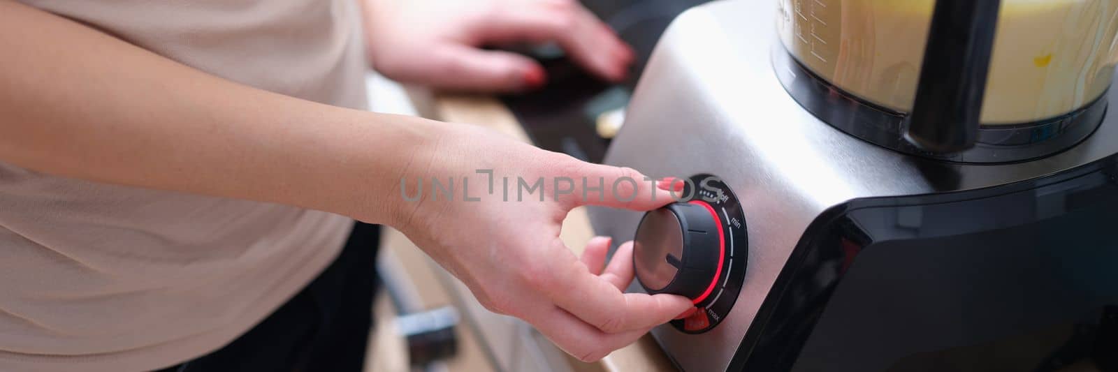 Woman turns on mixer with dough in kitchen. Kitchen appliances for chopping and mixing food