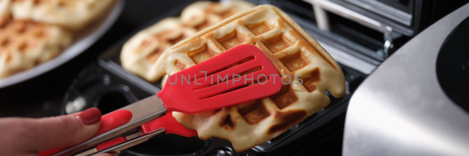 Pastry chef takes hot waffles from waffle iron in kitchen. Cooking sweet delicious dessert at home