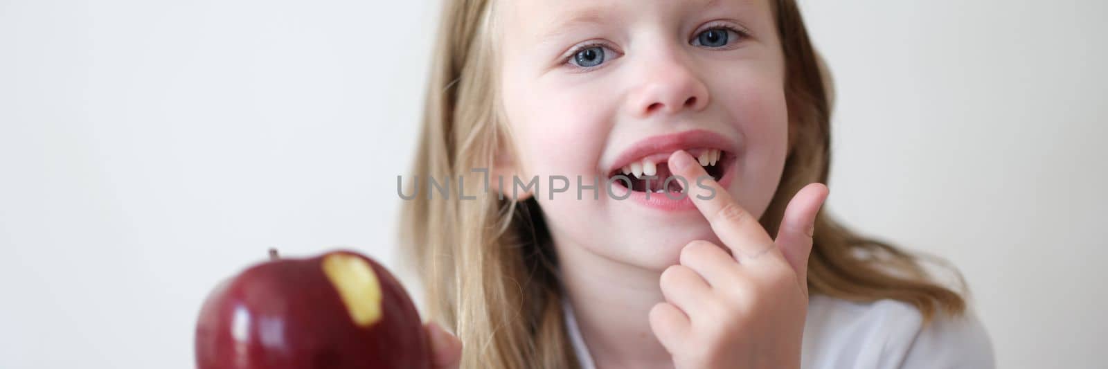 Portrait of smiling cute girl without teeth with red bitten apple in hand by kuprevich