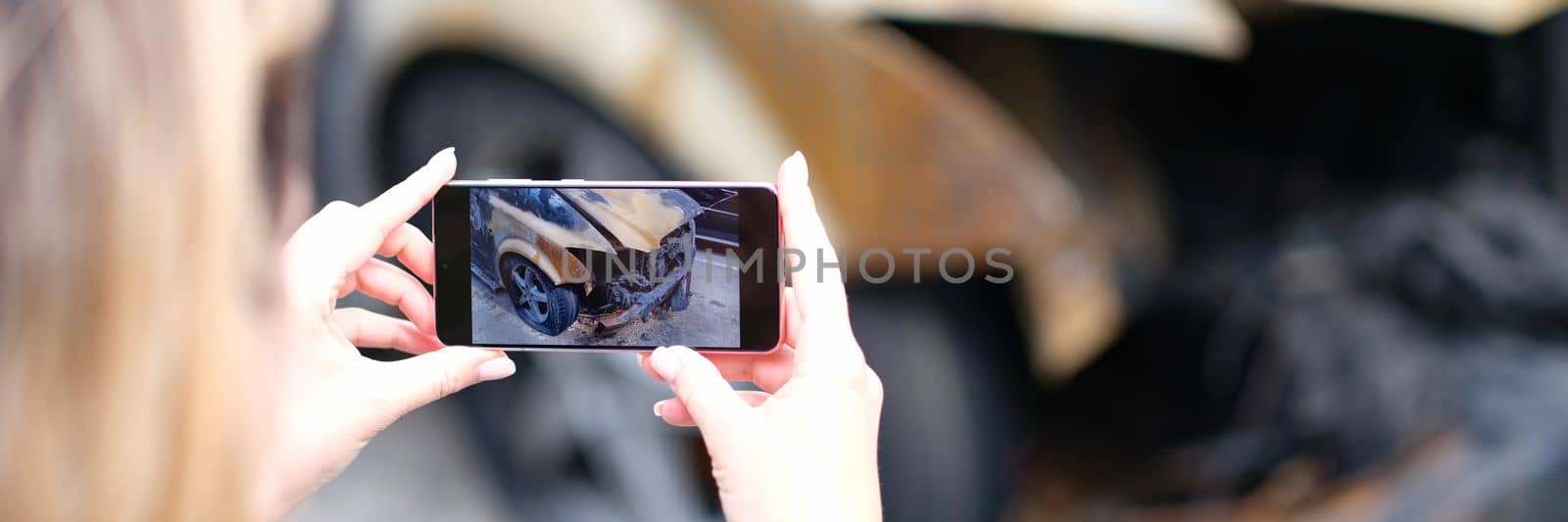 Closeup of female insurance broker taking photos of car after fire accident. The concept of damaged car and insured event