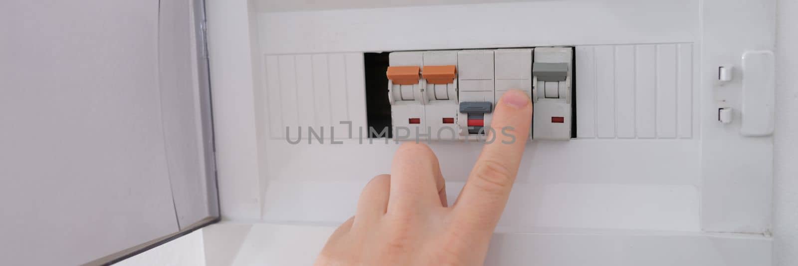 Many switches displayed on circuit breaker board. Fnger is about to turn it back on white