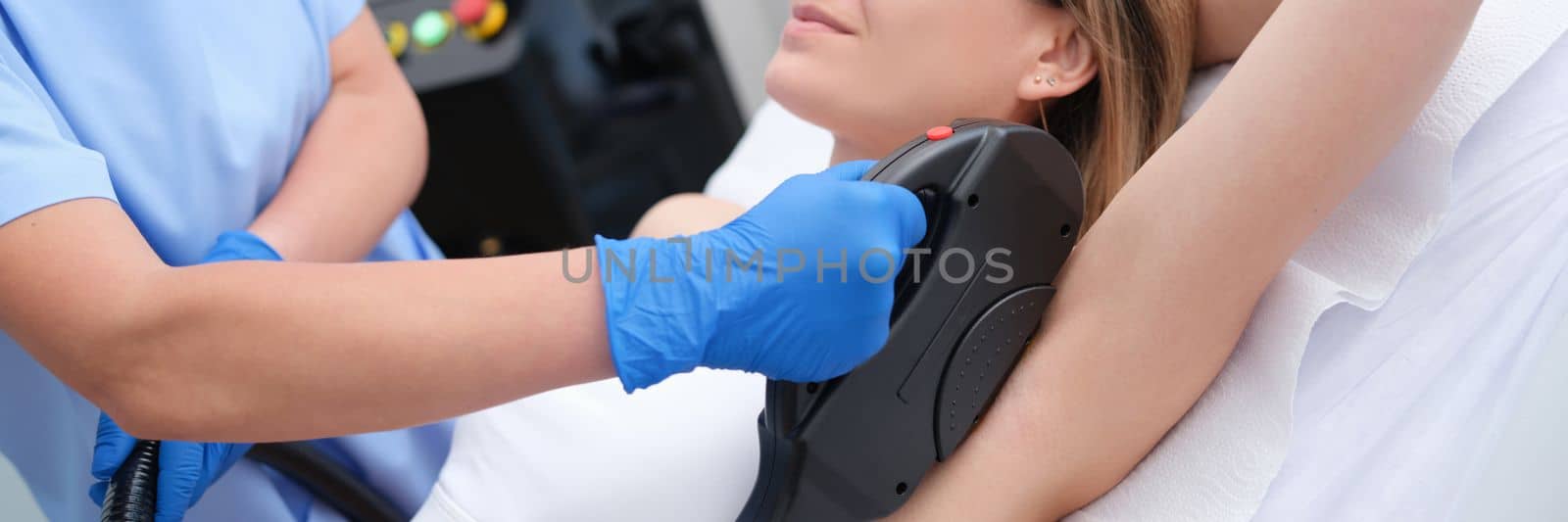 Woman undergoes hair removal procedure with photoepilator or laser hair removal of armpits in salon. Armpit laser hair removal concept