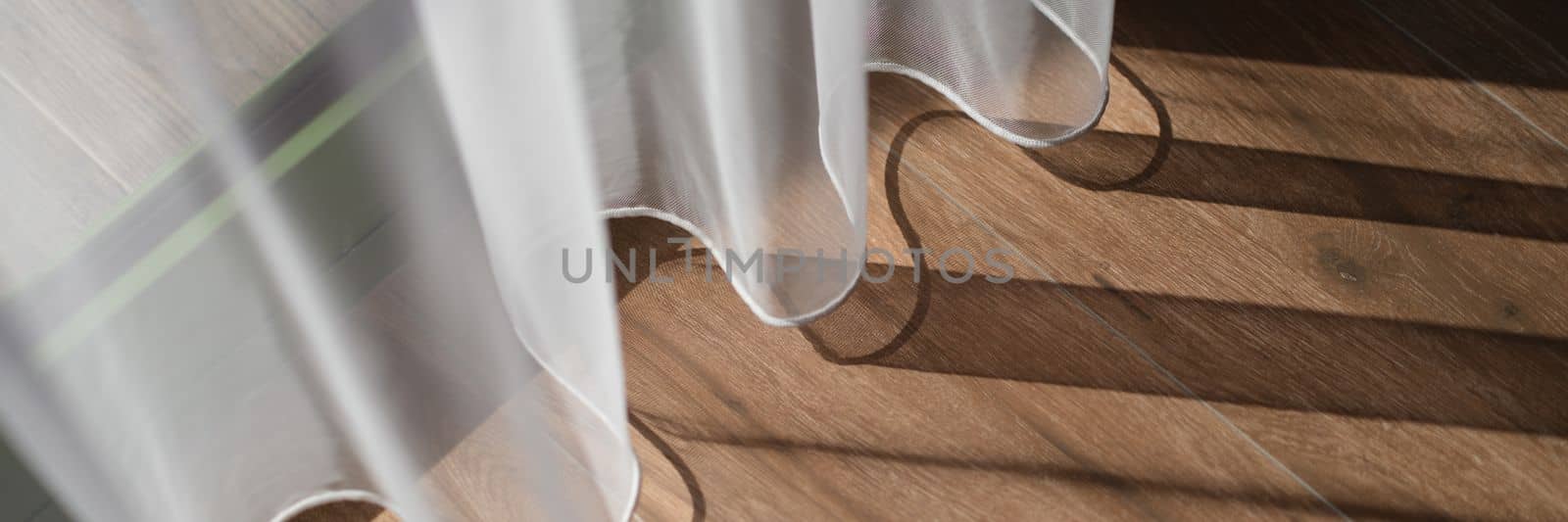 Closeup of light white curtains and brown wood laminate by window. Stylish home interior details