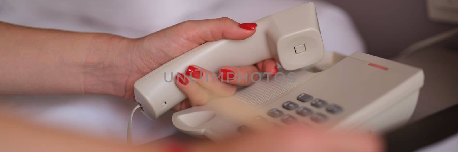 Woman picks up phone and dials number for room service in hotel closeup. Hotel service and call to reception concept