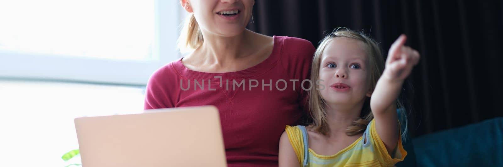 Portrait of mother and child sitting on sofa with laptop looking away in surprise. Emotions of surprise and delight