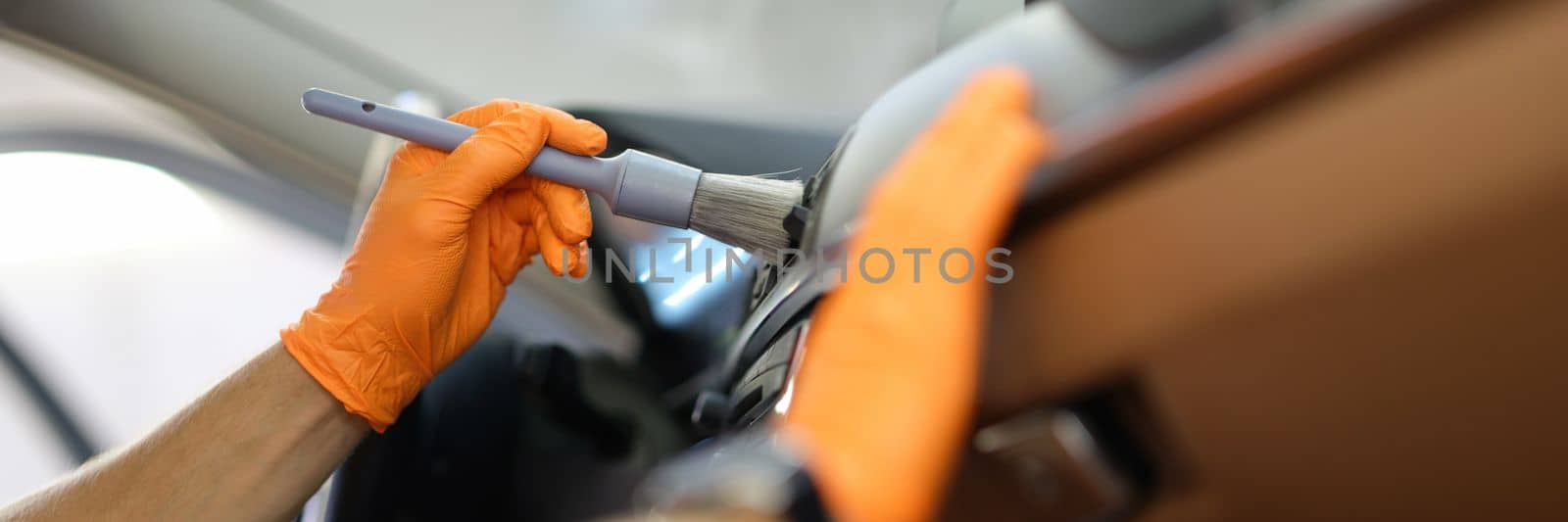 Master repairman cleans the car air conditioner with brush in workshop closeup. Dry cleaning of car interior concept