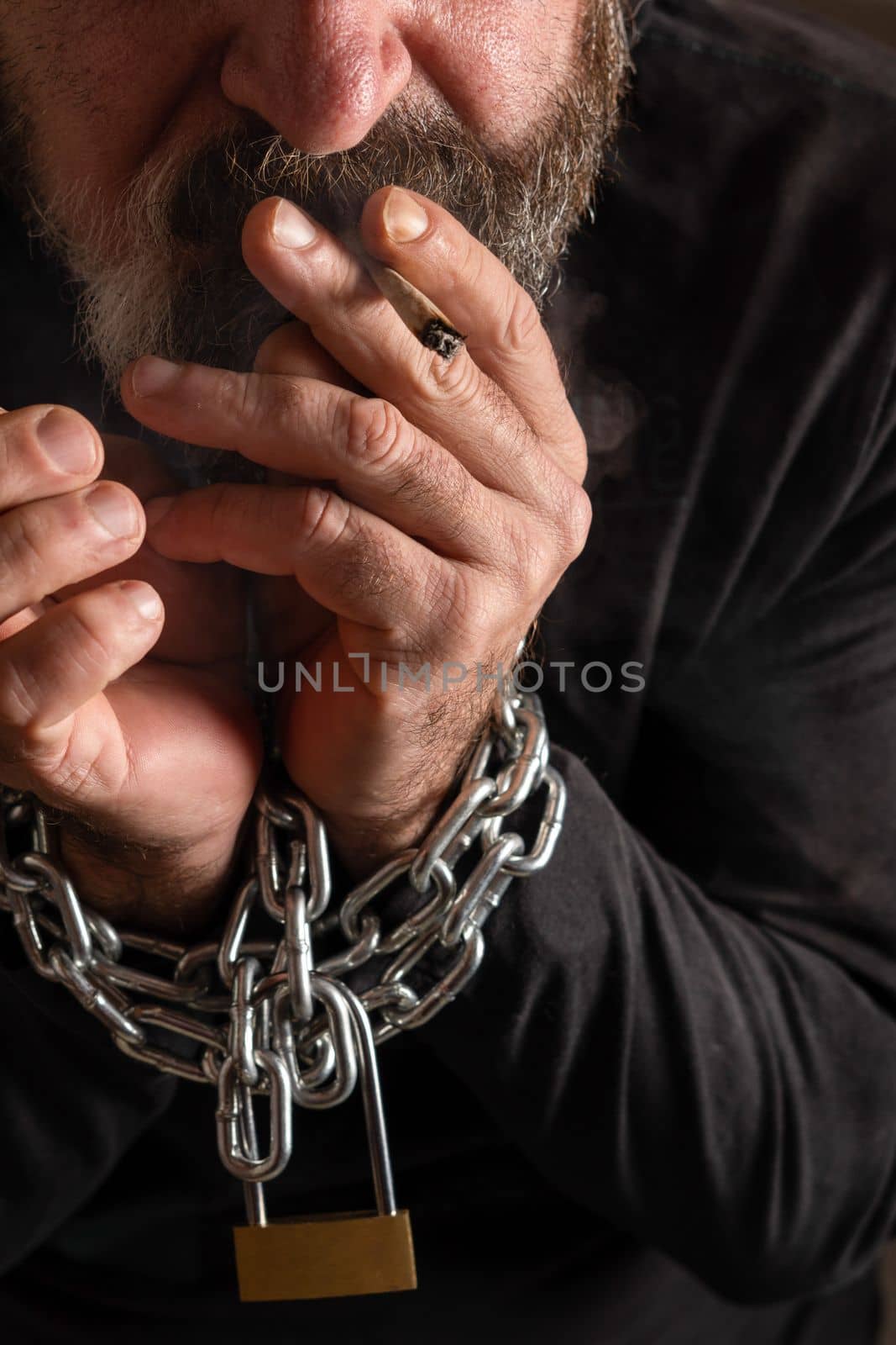 man with a cigarette in his mouth and his hands chained together, addiction concept, black background