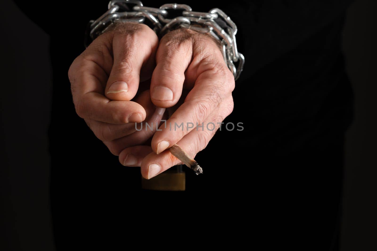 man's hands chained together, with a cigarette in his fingers , addiction concept by joseantona