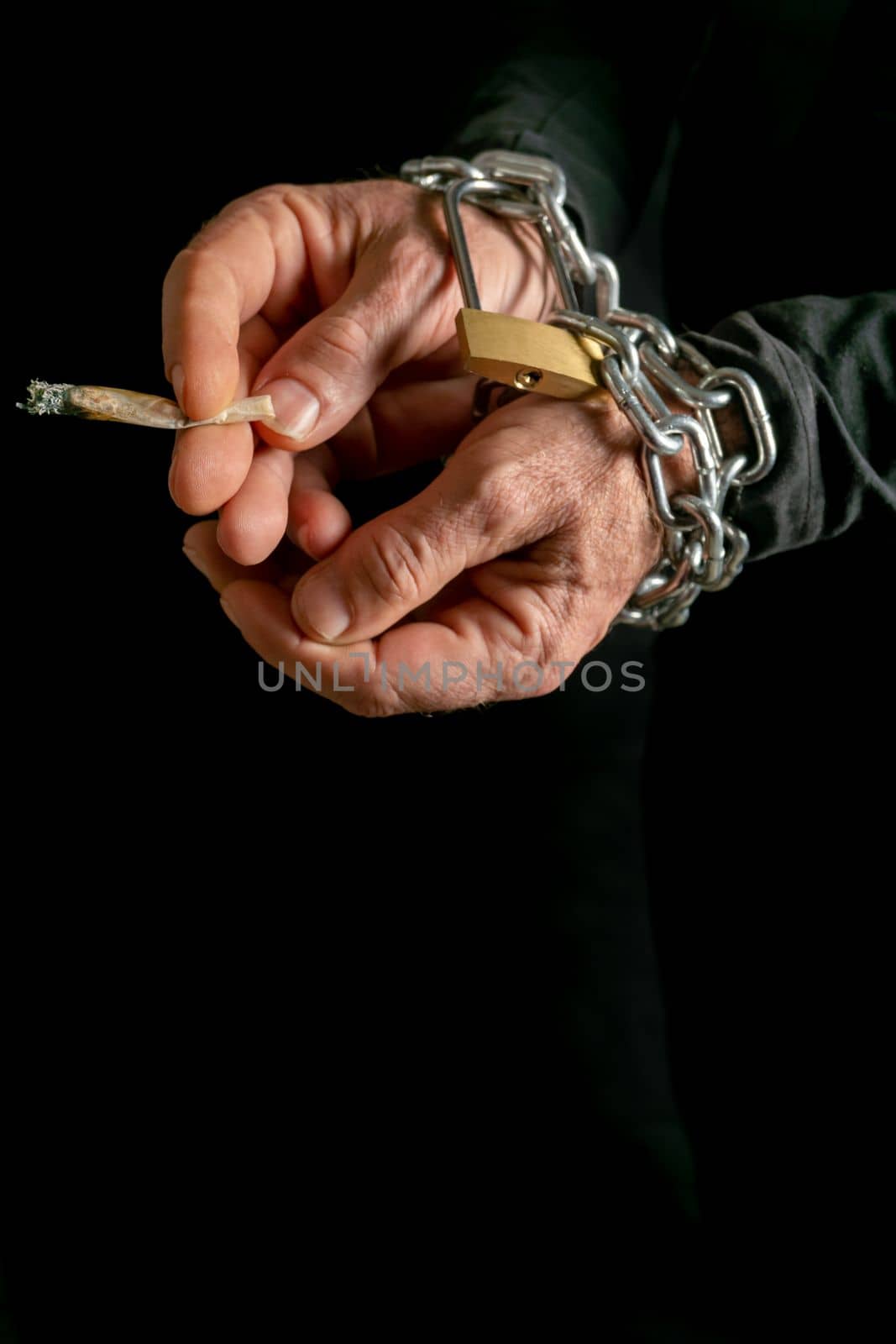 man smoking with chained hands on black background, concept of addiction