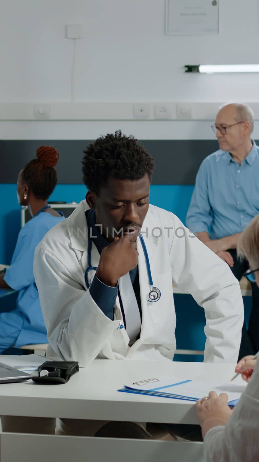 Doctor of african american ethnicity consulting old woman with sickness while sitting at desk in office. Senior patient signing checkup document files for healthcare appointment