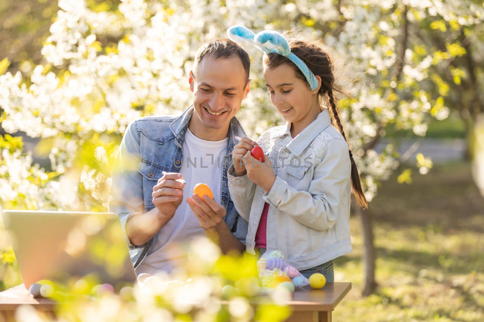 father and daughter coloring easter eggs with laptop in the garden by Andelov13