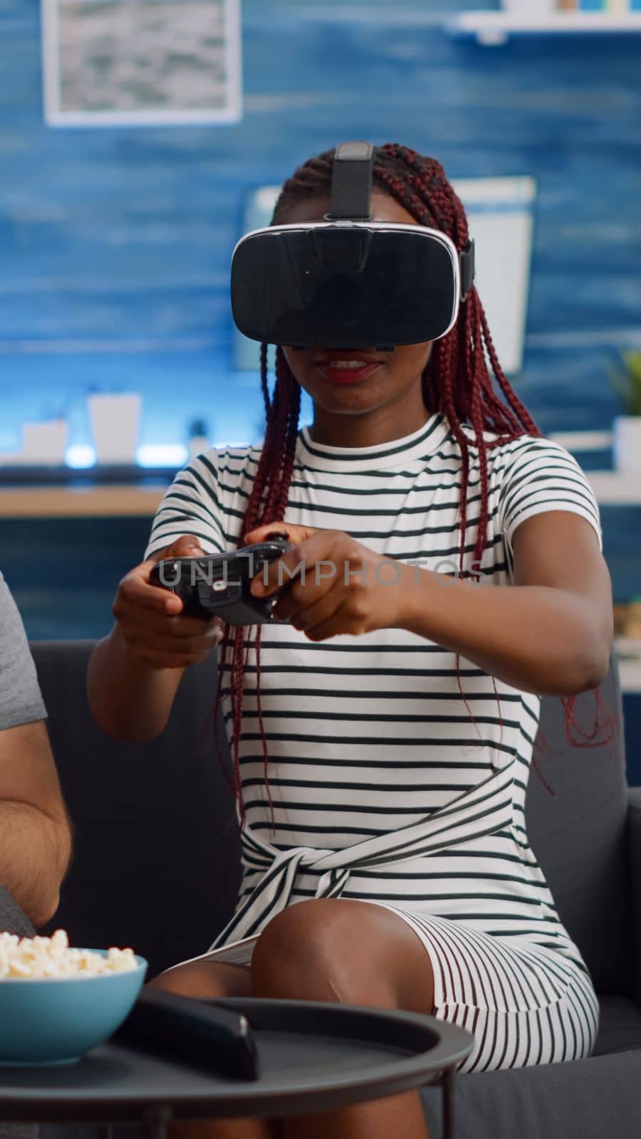 Married interracial couple using technology at home. African american woman with vr glasses playing game while caucasian man watching and cheering in living room. Mixed race cheerful people