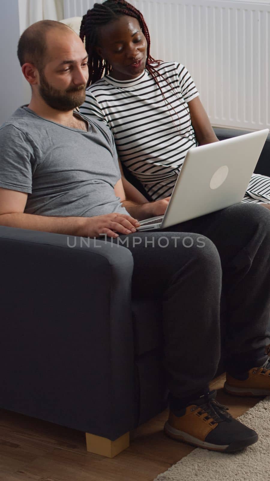 Modern interracial couple waving on video call conference sitting on sofa in living room. Young multi ethnic partners using online remote communication on laptop with internet connection