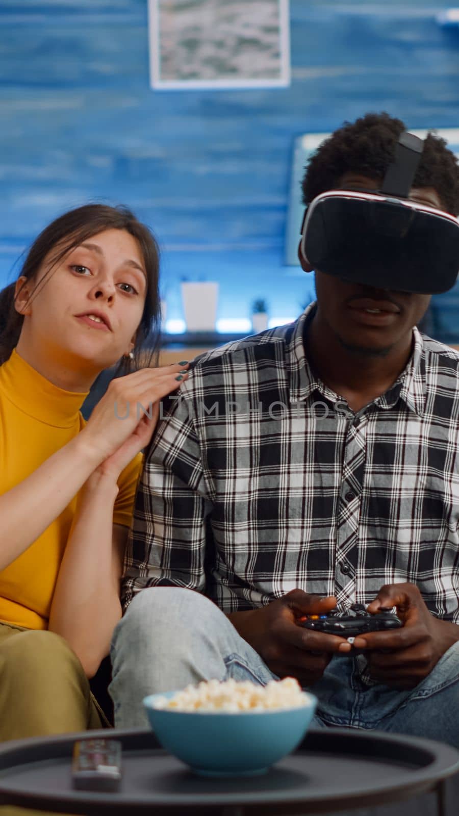 POV of interracial couple using technology for entertainment at home. African american man playing with vr glasses and controller for console while caucasian woman cheering and watching