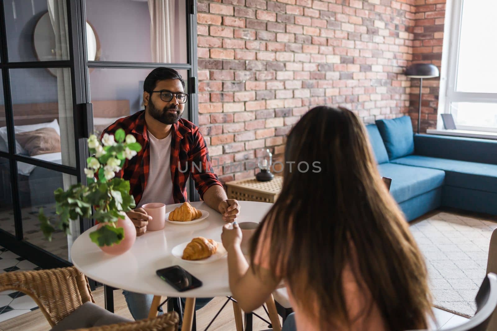 Young diverse loving couple eating croissant and talks together at home in breakfast time. Communication and relationship concept by Satura86