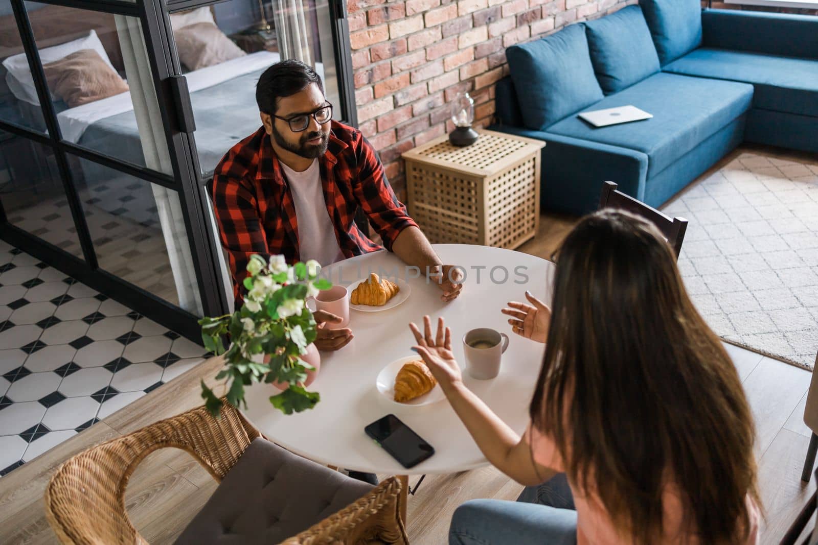 Young diverse loving couple eating croissant and talks together at home in breakfast time. Communication and relationship concept by Satura86